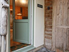 An open green door leading to a room with wooden walls and a lamp a carved wooden sculpture near the door a wooden door and a pet bowl on the floor at The Aqua Shack in Newquay