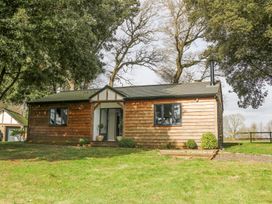 A single story wooden house with two black framed windows and a small porch surrounded by trees and grass at Holm Oaks Cottage in Busbridge near Godalming