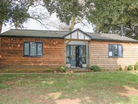 A wooden cottage with two windows and an open front door surrounded by trees at Holm Oaks Cottage in Busbridge near Godalming