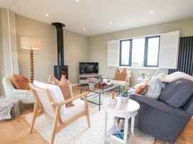 A living room with chairs a sofa a glass coffee table a floor lamp and a wood stove at Holm Oaks Cottage in Busbridge near Godalming