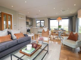 A living room with a gray sofa brown pillows glass coffee table and dining area with wooden chairs at Holm Oaks Cottage in Busbridge near Godalming