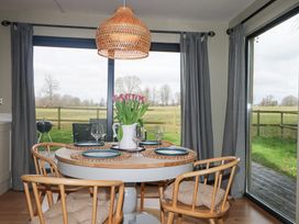 A dining area with a round table set with plates wine glasses and flowers with wooden chairs near large windows at Holm Oaks Cottage Busbridge near Godalming