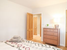 A bedroom with a bed covered with a patterned blanket and towels on top a brown chest of drawers with a lamp and a plant and wooden doors in Holm Oaks Cottage in Busbridge near Godalming