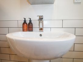 A white bathroom sink with a chrome faucet and two brown pump bottles on the tiled wall at Holm Oaks Cottage in Busbridge near Godalming