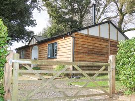 A wooden cottage with a gate and trees surrounding it at Holm Oaks Cottage in Busbridge near Godalming
