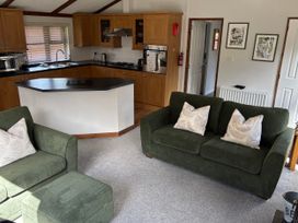 A living room with a green sofa and kitchen area at 2 Riverside Lodge Abercych near Cenarth