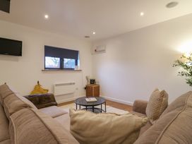 A living room with a beige sofa two cushions a round coffee table a small wooden cabinet a window with a closed blind and a wall-mounted television at Hub House in Three Oaks near Hastings