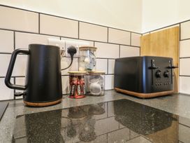A kitchen counter with a black kettle, jars of coffee and tea pods, and a black toaster with a wooden board in the background at Hub House in Three Oaks near Hastings