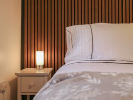 A bedside table with a lamp next to a bed with white linens and a wooden slatted headboard at Hub House in Three Oaks near Hastings