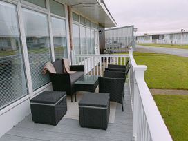 A patio with black wicker chairs and a table on a porch with white railings at The Chalet in Chapel St Leonards