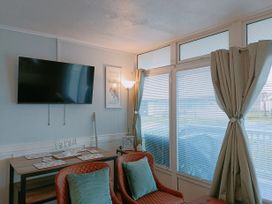 A living room with a wall-mounted TV two chairs with cushions a table and windows with curtains and blinds at The Chalet in Chapel St Leonards