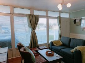 A sitting area with a sofa two chairs a coffee table and windows with curtains and blinds at The Chalet in Chapel St Leonards