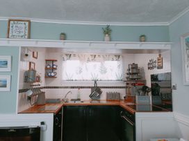 A kitchen with wooden countertops, a sink, toaster, stove, various utensils, and a window with patterned curtains at The Chalet in Chapel St Leonards