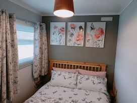 A bedroom with a wooden bed with butterfly patterned bedding and curtains and floral artwork on the wall at The Chalet in Chapel St Leonards