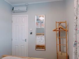 A bedroom door with an air conditioner above a wall mirror and a wooden clothes rack next to butterfly patterned curtains at The Chalet in Chapel St Leonards