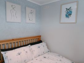 A bedroom corner with a wooden bed frame floral bedding and three framed artworks on blue and white walls at The Chalet in Chapel St Leonards