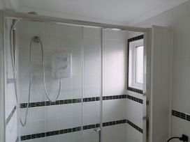 A bathroom shower area with white tiles and black tile accents and a small window at The Chalet in Chapel St Leonards