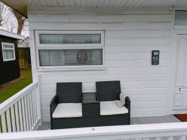 A porch with two black chairs with white cushions and a small table between them at The Chalet in Chapel St Leonards