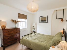 A bedroom with a bed with green bedding a wooden chest of drawers a window and a standing mirror at Launchers Cottage in Scarborough