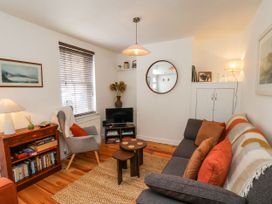 A living room with a gray sofa with orange pillows a gray armchair wooden coffee tables a television on a small stand and bookshelf at Launcher's Cottage in Scarborough