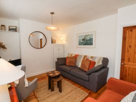 A living room with a gray sofa with pillows and a throw a round mirror on the wall a wooden door and a small nesting coffee table at Launcher's Cottage in Scarborough