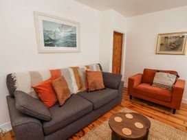 A living room with a gray sofa and orange armchair with cushions a wooden round coffee table and two framed pictures on the walls at Launcher's Cottage in Scarborough