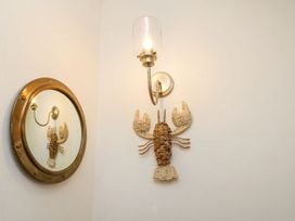 A wall with a round mirror and a wall light above a woven lobster decoration at Launcher's Cottage in Scarborough