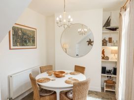 A dining room with a round table and four wicker chairs a large round mirror a chandelier and shelves with decorations at Launcher's Cottage in Scarborough