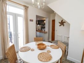 A dining room with a round white table and wicker chairs near glass doors and an adjacent kitchen at Launcher's Cottage in Scarborough