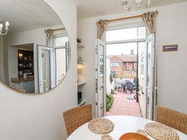 A dining area with a round table and wicker chairs opening to a patio with outdoor furniture at Launcher's Cottage in Scarborough