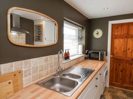 A kitchen with a wooden countertop a stainless steel sink a microwave a window with blinds a wooden cutting board a wall clock and a wooden door at Launcher's Cottage in Scarborough