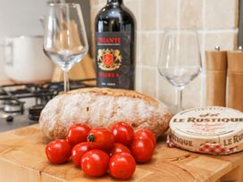 A kitchen countertop with a loaf of bread cherry tomatoes a cheese container a bottle of Chianti wine and two wine glasses at Launcher's Cottage in Scarborough