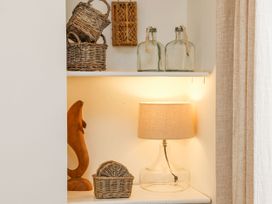 A shelf with wicker baskets, glass bottles, a wooden dolphin sculpture, and a glass lamp with a fabric shade at Launcher's Cottage in Scarborough
