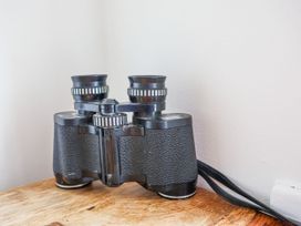 A pair of vintage black binoculars on a wooden surface against a white wall at Launchers Cottage in Scarborough