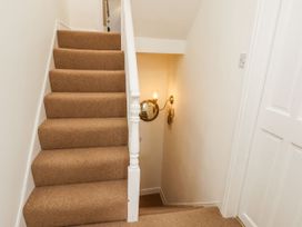 A staircase with beige carpet and white banister next to a wall with a round mirror and a wall light at Launcher's Cottage in Scarborough