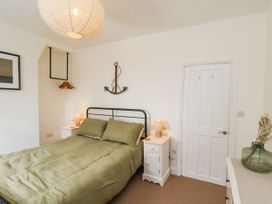 A bedroom with a bed with green bedding two white bedside tables with lamps a door an anchor wall decoration and a hangers on a rack at Launcher's Cottage in Scarborough