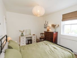 A bedroom with a bed with green bedding a white dresser a wooden chest of drawers and a window with a blind at Launcher's Cottage in Scarborough