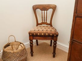A wooden chair with a polka dot upholstered seat beside a woven basket with rolled towels in a corner at Launcher's Cottage in Scarborough