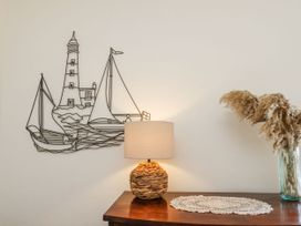 A wooden table with a lamp and a vase with dried plants with a wire art of lighthouse and sailboats on wall at Launcher's Cottage in Scarborough