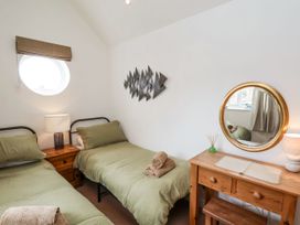 A bedroom with two single beds a wooden bedside table with a lamp a wooden dressing table with a round mirror and a stool at Launcher's Cottage in Scarborough