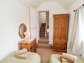 A bedroom with two single beds, a wooden dresser with a mirror, a lamp, a wooden wardrobe, and a staircase visible through an open door at Launcher's Cottage in Scarborough