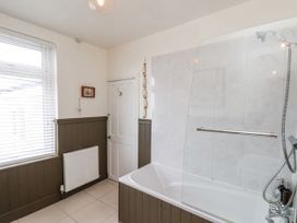 A bathroom with a bathtub and shower, a window with blinds, a radiator and a door at Launcher's Cottage in Scarborough