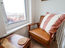 A corner with a brown leather armchair with a striped cushion beside a window and a wooden table with a coaster at Launcher's Cottage in Scarborough