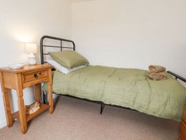 A bedroom with a single bed with green bedding and a wooden bedside table with a lamp at Launcher's Cottage in Scarborough