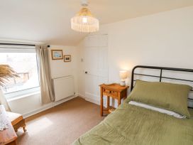 A bedroom with a bed with green bedding a wooden nightstand with a lamp a window with curtains and framed pictures on the wall at Launcher's Cottage in Scarborough