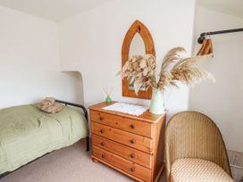 A bedroom with a single bed green bedding wooden dresser wicker chair and a mirror at Launchers Cottage in Scarborough