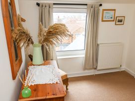 A small room with a wooden table, a vase with dried pampas grass, a window with curtains, a radiator, and two framed pictures on the wall at Launchers Cottage in Scarborough