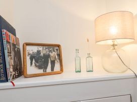 A shelf with books a framed black and white photo two small glass bottles and a table lamp at Launcher's Cottage in Scarborough