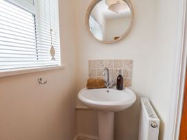 A small bathroom with a pedestal sink a round mirror beige tiles a window with blinds and a radiator at Launcher's Cottage in Scarborough
