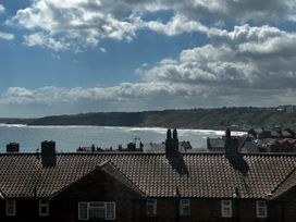 Rooftops of houses with tiled roofs and chimneys by a coastline with sea and hills under a cloudy sky in Scarborough